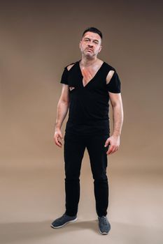 Against a gray background stands a battered angry man in a black T-shirt with wounds.