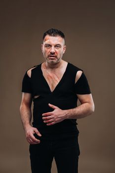 Against a gray background stands a battered angry man in a black T-shirt with wounds.