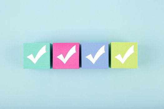 Four checkmarks on multicolored cubes in a row on blue background with copy space. Concept of questionary, checklist, to do list, planning, business or verification. Modern minimal composition 