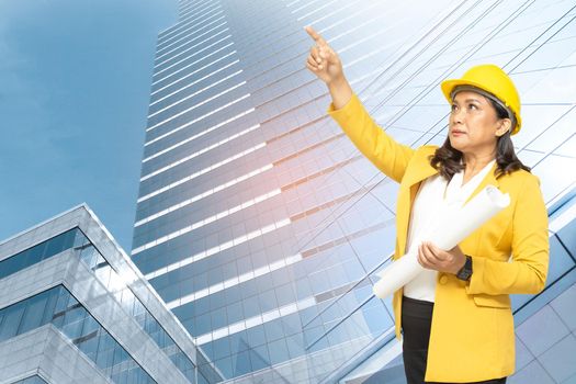 Asian engineer woman with blueprint standing at building background with copy space, engineering construction and architecture concept.