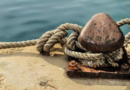 Rusty mooring bollard with tied rope in the port of Santa Pola, Alicante, Spain