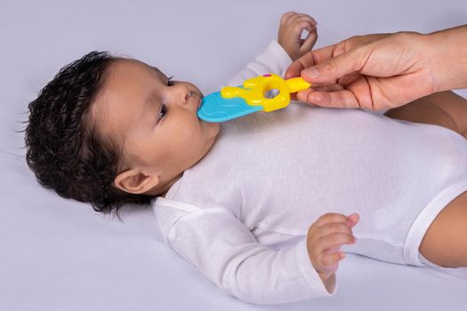 Infant lying on his back and one hand putting a toy in his mouth