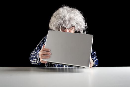 An elderly man does not know how to use the computer. He holds the laptop in his hand without knowing how to turn it on