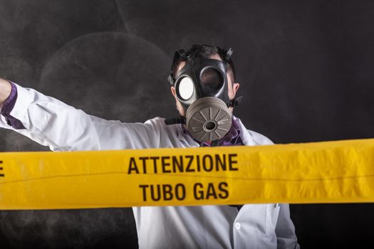 A medical engineer wearing antigas mask experienced in the gas leaks crisis directing the emergency during the chaos. On the yellow tape the written notice "attention gas tube"