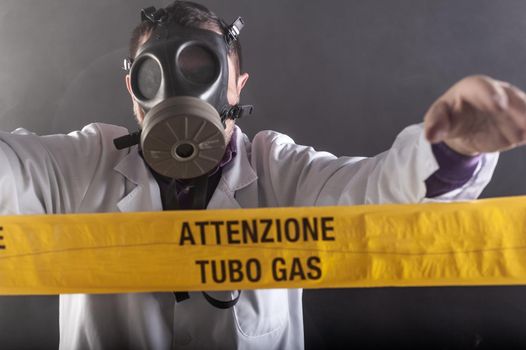 A medical engineer wearing antigas mask experienced in the gas leaks crisis directing the emergency during the chaos. On the yellow tape the written notice "attention gas tube"