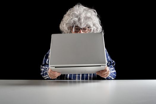 An elderly man does not know how to use the computer. He holds the laptop in his hand without knowing how to turn it on