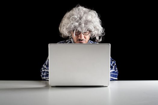 A boomer senior-focused concentrated sit at the desk looking at laptop computer on black background