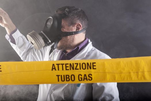 A medical engineer wearing antigas mask experienced in the gas leaks crisis directing the emergency during the chaos. On the yellow tape the written notice "attention gas tube"