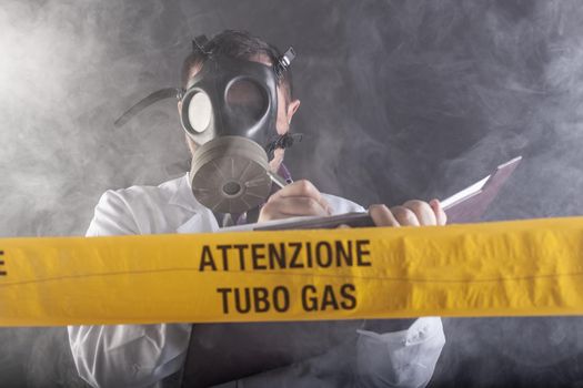 A medical engineer wearing antigas mask experienced in the gas leaks crisis directing the emergency during the chaos. On the yellow tape the written notice "attention gas tube"