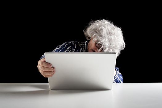 An elderly man does not know how to use the computer. He holds the laptop in his hand without knowing how to turn it on