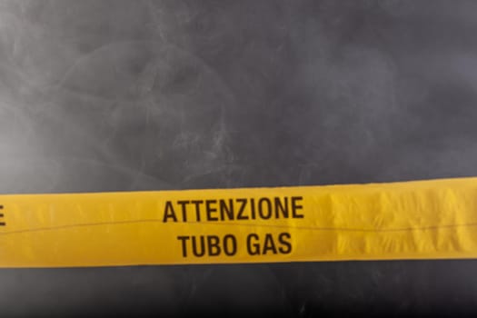 Yellow emergency sign of attention gas pipe on smoke-filled background. On the yellow tape the written notice "attention gas tube"