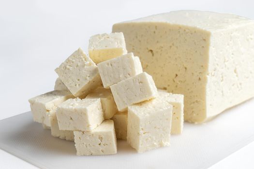 White cheese cut into several pieces on a white surface and white background