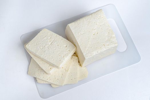 White cheese cut into several pieces on a white surface and white background