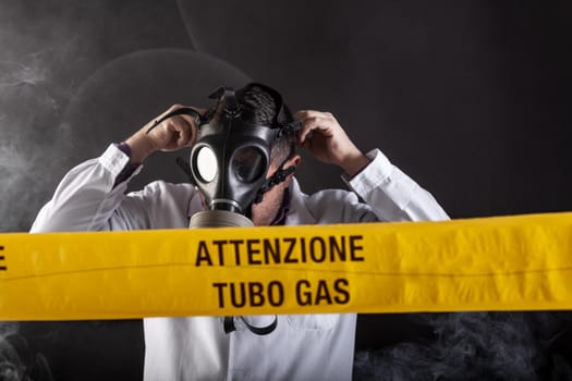 A medical engineer wearing antigas mask experienced in the gas leaks crisis directing the emergency during the chaos. On the yellow tape the written notice "attention gas tube"