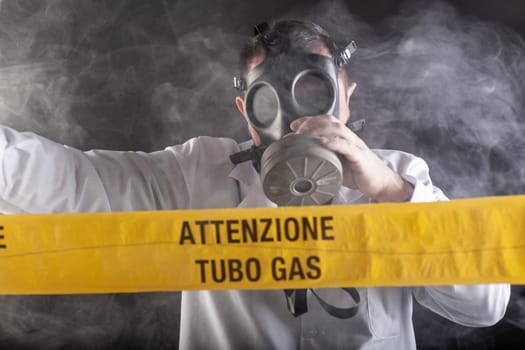 A medical engineer wearing antigas mask experienced in the gas leaks crisis directing the emergency during the chaos. On the yellow tape the written notice "attention gas tube"