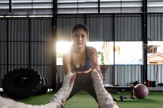 Attractive strong asian fitness woman doing battle ropes exercise at gym. weight training exercise session.