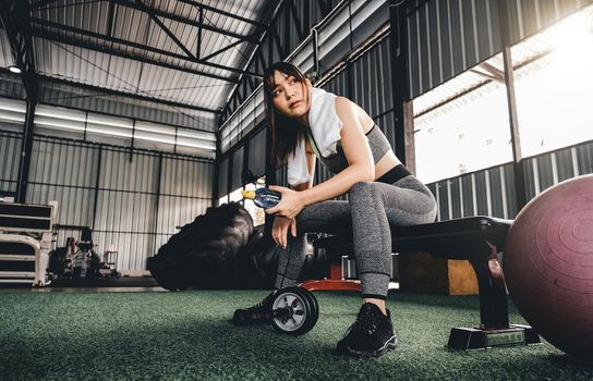 Attractive fitness woman sitting on a chair and resting after workout at fitness centre. Female take a break after hard cardio.