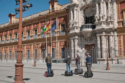 April 2019 - peoples on scooter electric skateboard intelligent hoverboard alternative way if visiting the city and view of San Telmo Palace, Seville, Spain. Seat of the presidency in a sunny day