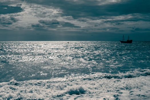 Seascape. A sailing ship is sailing on the sea against the backdrop of a dark sky with a dramatic atmosphere. Dark blue toning.