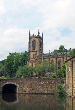 a stone bridge crossing the canal in sowerby bridge west yorkshire with the historic christ church building surrounded by trees