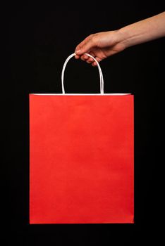 close up hand holding red shopping bag black background. High resolution photo
