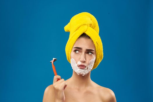 cheerful woman with a yellow towel on his head shaving blue background. High quality photo
