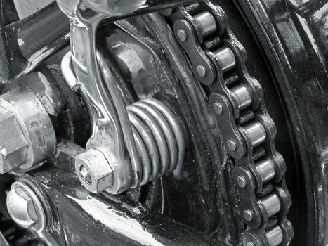 monochrome close up of the drive chain on a black vintage motorbike with chrome fixtures and steel bolts