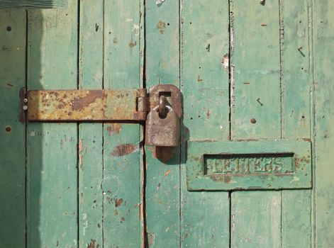 close up of an old wooden door with green faded paint and a rusty closed padlock and old metal letterbox