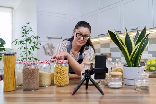 Housewife woman blog, female recording video reviewing products on smartphone at home in the kitchen. Blogging, vlog, technology, lifestyle, hobbies and leisure, people concept