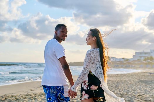 Portrait of beautiful young multiracial couple holding hands on beach. Happy loving african man and asian woman walking together. People love relationship multiethnic family, vacation, tourism concept