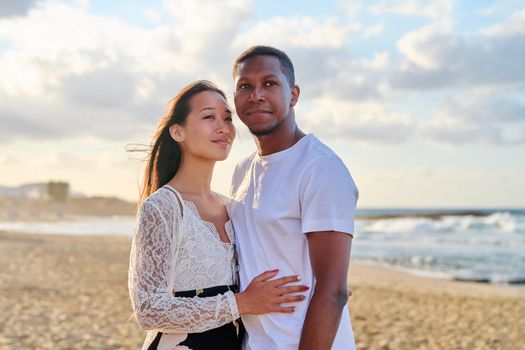 Portrait of happy young beautiful couple on beach. Interracial couple, african american man and asian woman embracing at seaside. People, relationships, dating, vacation, tourism, multi-ethnic family