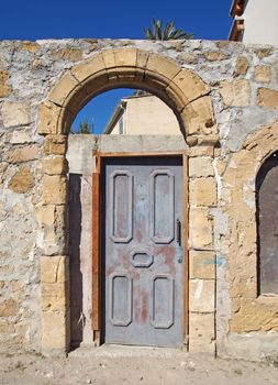 an old wooden door in an arched frame in an ancient stone wall on a sunlit street in nicosia cyprus