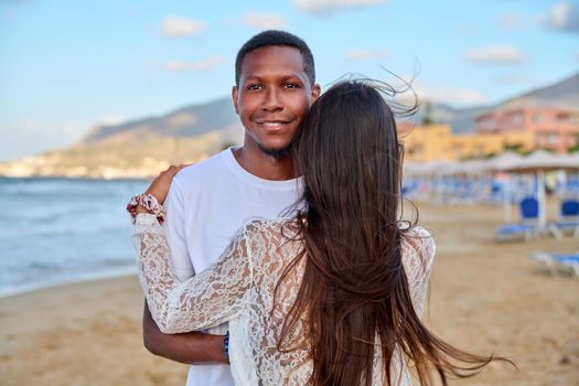 Happy young couple hugging, man's face close up. Multiracial couple, african american man looking at camera on summer beach, relationship, love, happiness, people, multiethnic family, tourism, travel