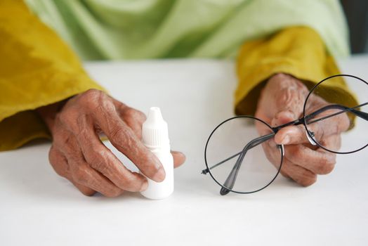 senior women hand holding a eye dropper on table .
