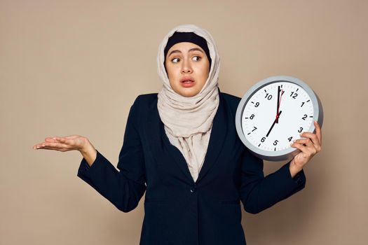 woman in hijab with clock in hands work office beige background. High quality photo