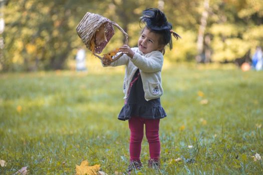 little cute witch playing with a basket of leaves in the autumn park