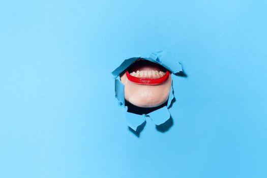 woman peeping through the holes in the poster blue studio background. High quality photo