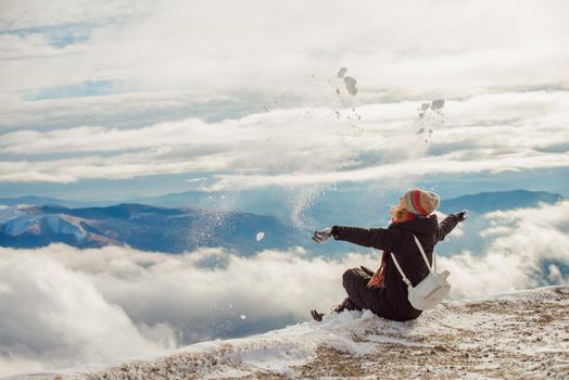 Hiking girl scattering snow and enjoy the fresh snow on a beautiful winter day in the mountains, the top of the mountain through the clouds in the background. Cold frozen winter activities. The concept of outdoor lifestyle happiness. High quality photo