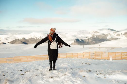 The woman with outstretched arms and colorful scarf and hat, looking at the beautiful view of the mountains on a very sunny winter day and clear blue sky. Lifestyle happiness mood in the mountains