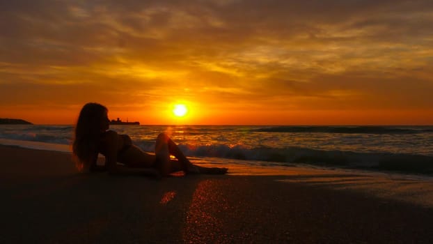 Woman with long hair lying on the sand looking at the sea and waves Enjoy the sea breeze in the morning. Colorful summer landscape.