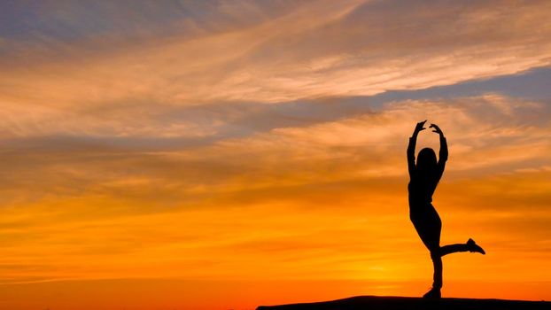Silhouette of woman with arms raised in a ballerina position, on a very beautiful sunset background. An image that conveys positivism.