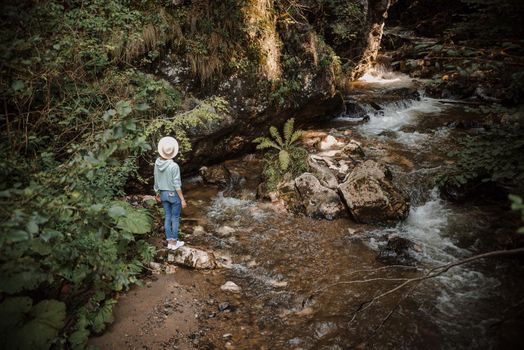 Young tourist woman hiking by mountain river enjoying landscape. Traveler walking along rocks. Summer vacation. High quality photo