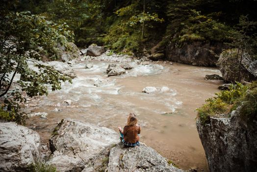 Young woman practicing yoga breathing and meditation in harmony with nature. Standing on the edge of a waterfall on a forest river, on a huge rock. Atmospheric green forest at the foot of the mountains. High quality photo