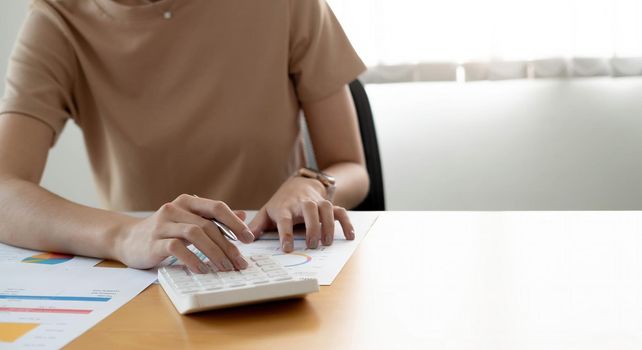 Close up woman using calculator and laptop for do math finance on wooden desk in office and business working background, tax, accounting, statistics and analytic research concept..