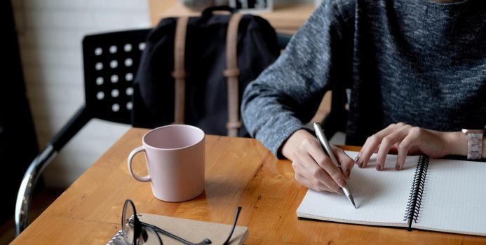 Cropped photo hand of woman writing making list taking notes in notepad working or learning online with laptop at home.