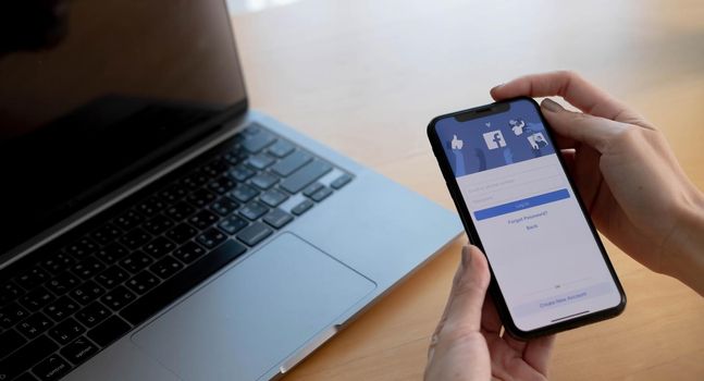 CHIANG MAI ,THAILAND AUG 18 2021 : Woman holding a iPhone X with social Internet service Facebook on the screen...