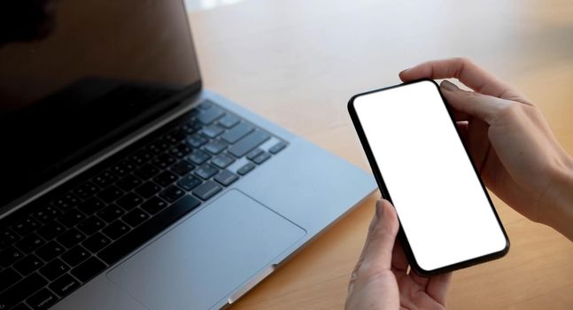 Mockup image blank white screen cell phone.women hand holding texting using mobile on desk at home office...