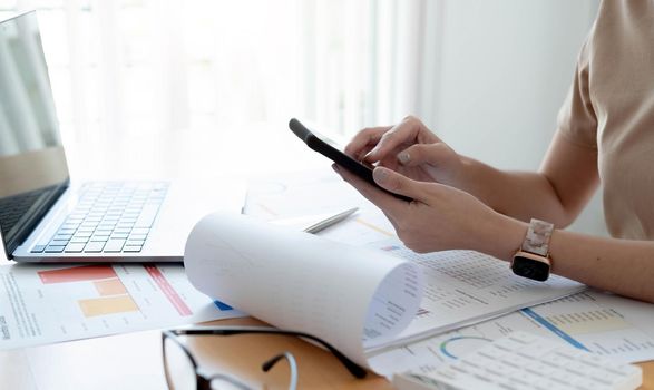 Close up hanf of woman using mobile phone and analysis the financial report paperwork in home office.