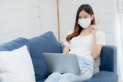 Young asian business woman in face mask think idea and work from home on laptop computer online to internet in living room, girl in medical mask and quarantine for covid-19, stay home, new normal.