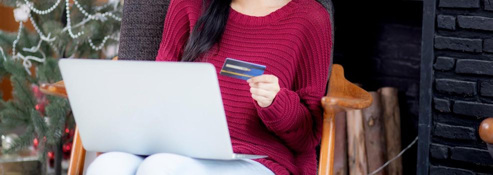 Young asian woman online shopping in Christmas with credit card on laptop computer, female buying and payment with debit card, xmas in holiday, happy new year, customer with purchase to internet.